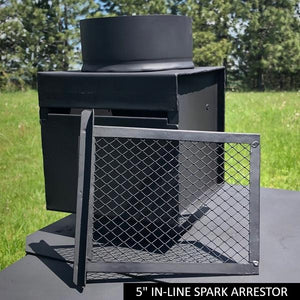 Black 5-inch inline spark arrestor for canvas tent stove pipe displayed on a metal surface with grassy field and trees in the background.