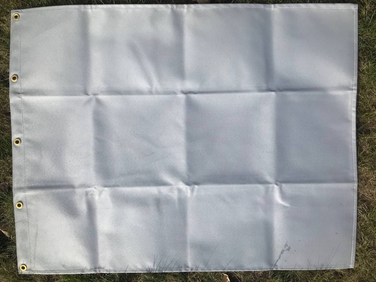 A gray canvas tent heat shield with metal grommets, laid out on a grassy surface.