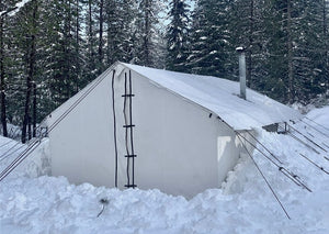 A white heavy duty canvas tent with a stove jack, set up in a snowy outdoor environment.