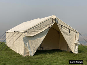 Canvas cook shack attached to a wall tent with grass campsite and clear sky background
