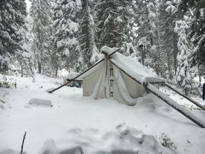 Snow-covered tent in a forest with trees in the background